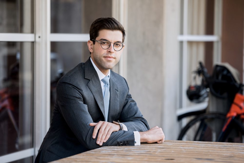 _ATL1979-Edit Corporate type of portrait of a man, sitting. He is wearing a gray suit, white shirt and a tie. Outdoors, on a terrace. Half body crop.