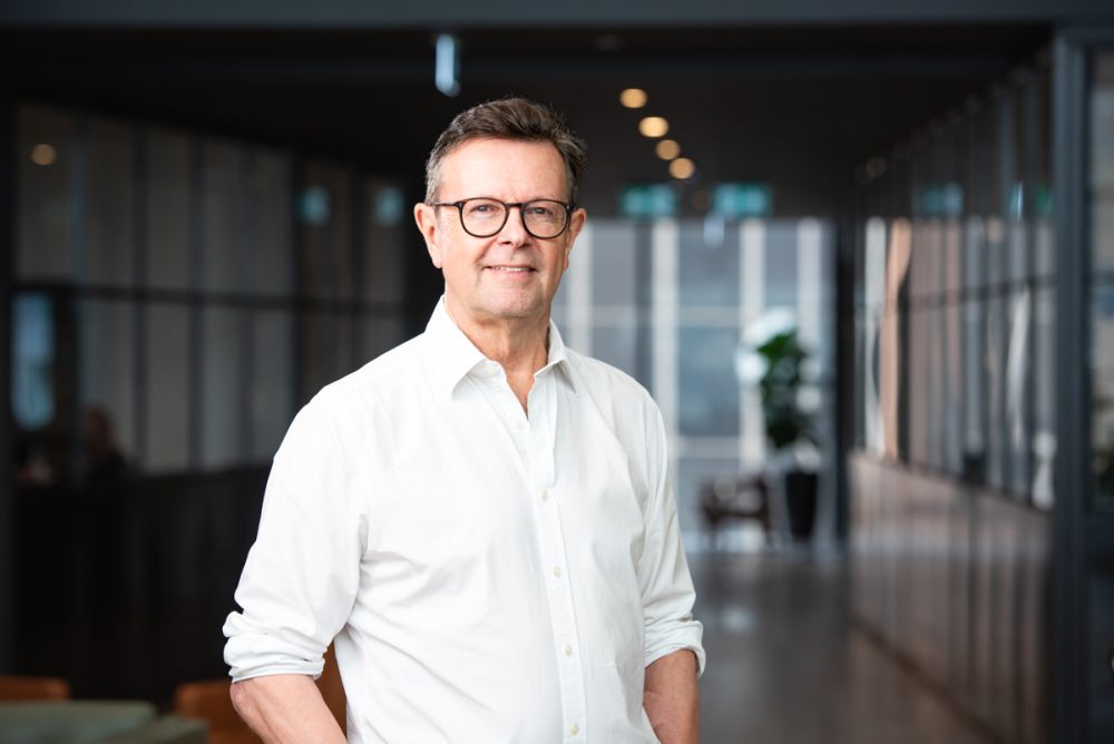 Scott_Paul Man in a white shirt, standing in an indoor environment. Soft light portrait and casual mood.